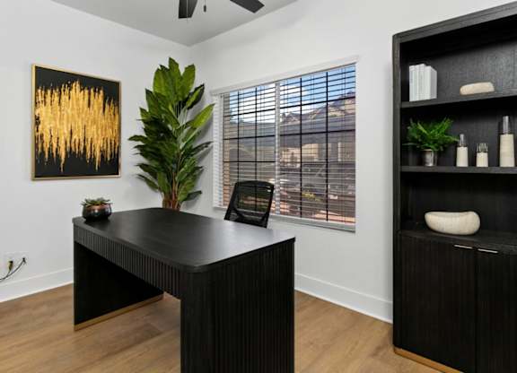 A black and gold abstract painting hangs on a white wall above a black desk.