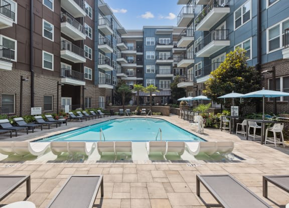 an outdoor swimming pool with lounge chairs and umbrellas in front of an apartment building