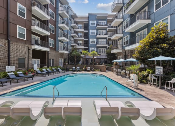 an outdoor swimming pool with lounge chairs and umbrellas in front of an apartment building
