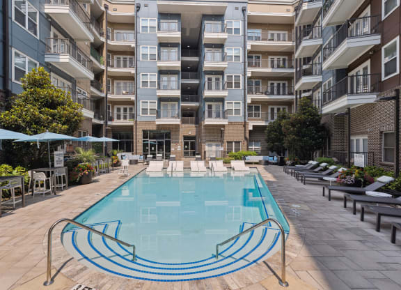 an outdoor swimming pool with lounge chairs and umbrellas in front of an apartment building