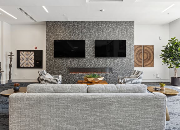 a living room with a gray couch and two televisions on the wall