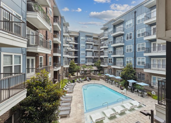 an outdoor pool with lounge chairs and umbrellas in front of an apartment building