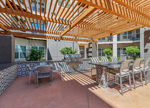 A patio with a table and chairs under a wooden pergola.