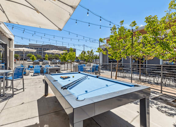 A pool table is in the middle of a patio with chairs around it.