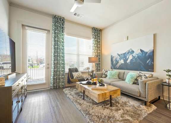 A living room with a grey couch and a large mountain painting on the wall.