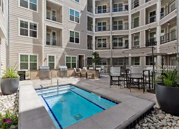 A small pool in a courtyard surrounded by chairs and plants.