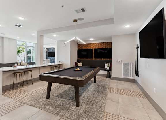 A room with a pool table and bar stools.