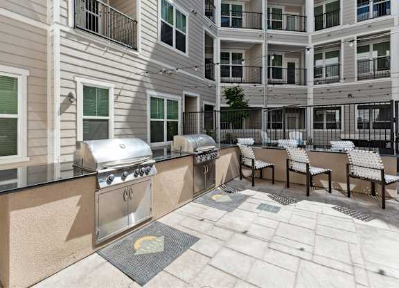A patio with a grill and chairs is surrounded by apartment buildings.