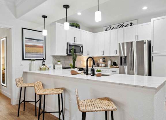 A kitchen with white cabinets and a white island with two barstools.