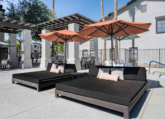 Two black couches are placed under orange umbrellas on a patio.