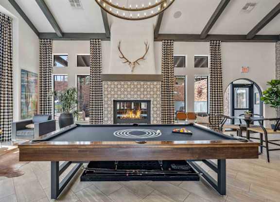 A pool table is in the middle of a room with a fireplace and a deer head mounted on the wall.