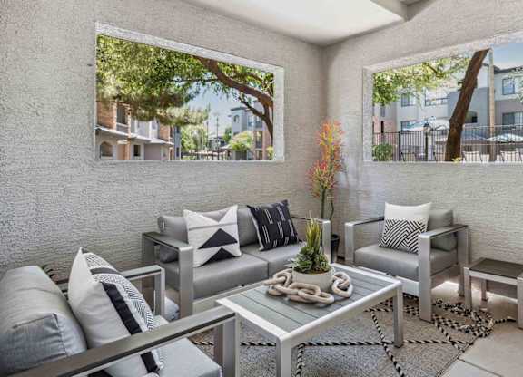 A modern outdoor patio with a glass table and grey couches.