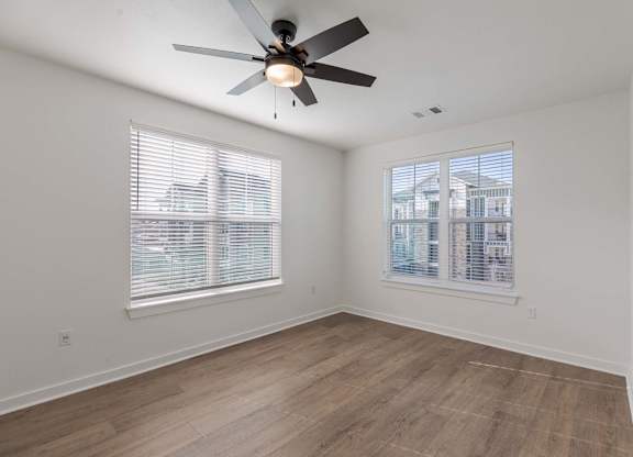 A room with a ceiling fan and two windows.