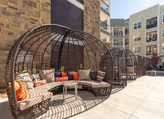 A patio with a large woven chair and a couch with pillows.