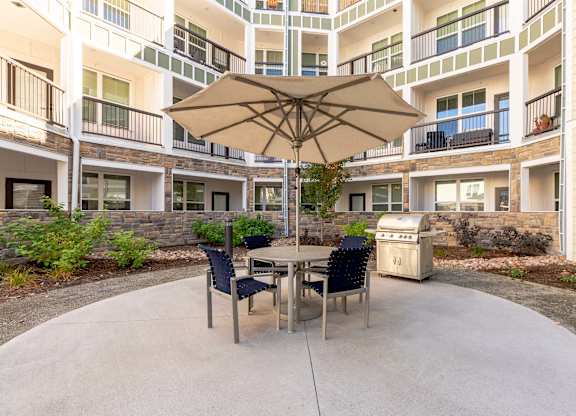A patio with a table and chairs and an umbrella in front of apartment buildings.