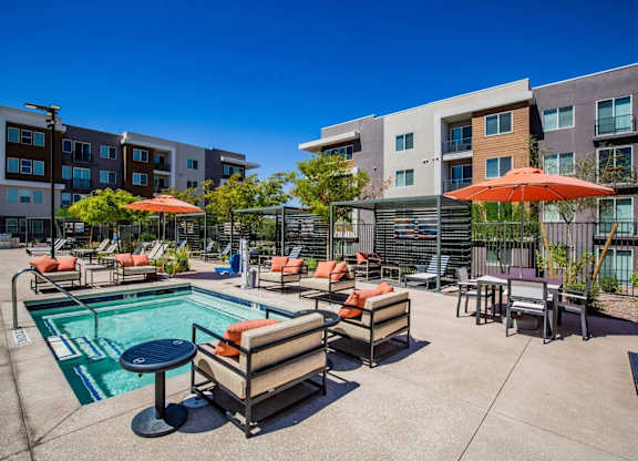 A pool area with chairs and umbrellas in front of apartment buildings.