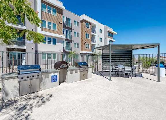 A modern apartment complex with a communal outdoor area featuring a grill and seating.