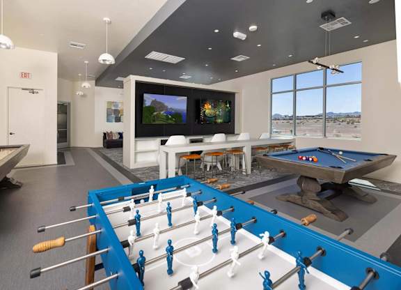 A foosball table is in the middle of a room with a pool table and a TV.
