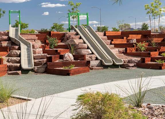 A playground with a green slide and a grey ramp.