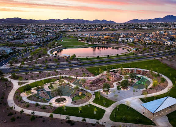 A park with a playground and a pond is surrounded by a city.