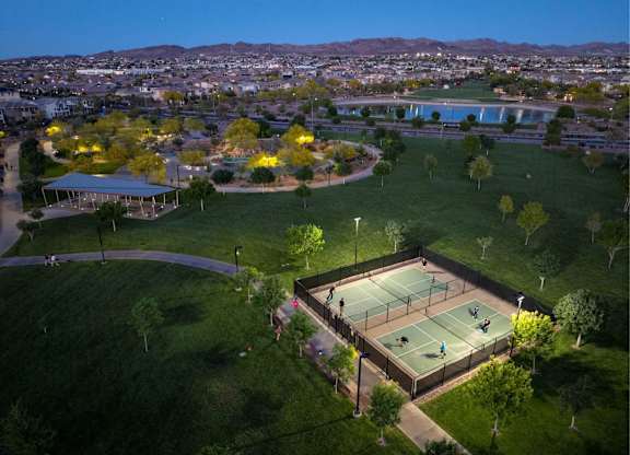 Tennis court surrounded by green grass and trees with people playing.