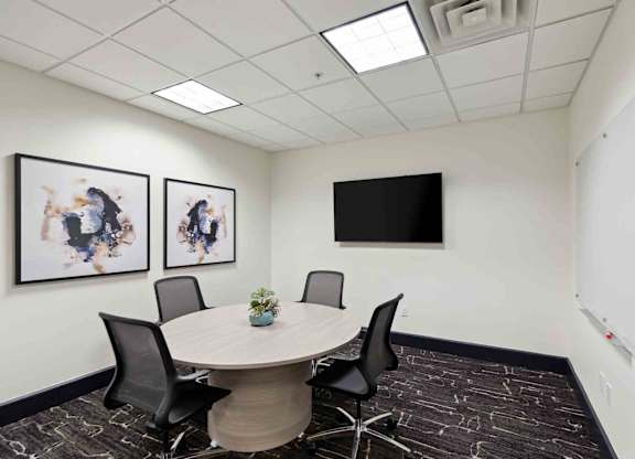 a meeting room with a round table and chairs and a flat screen tv on the wall