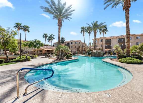 A large swimming pool surrounded by palm trees and apartment buildings.