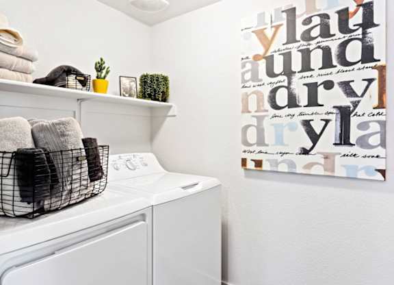 A laundry room with a washer and dryer, a basket of towels, and a wall art with the word