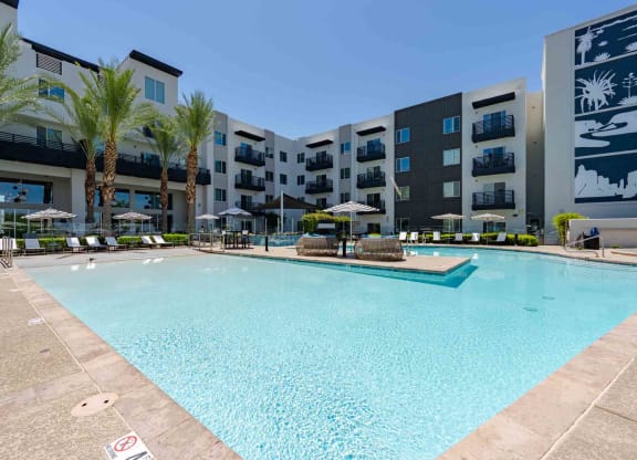 a large swimming pool with umbrellas and chairs in front of an apartment building