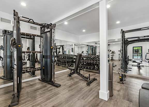 A gym with a variety of equipment including a squat rack, bench press, and a mirror.