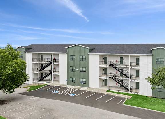A large white and green apartment complex with a parking lot in front.