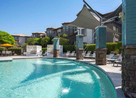 a swimming pool with lounge chairs and umbrellas in front of an apartment building