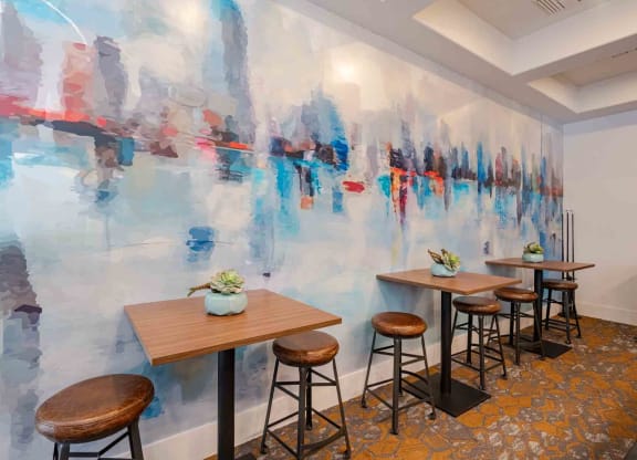 a room with a large painting on the wall and wooden tables and stools in front of