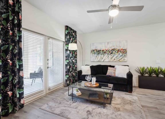 a living room with a black couch and a glass coffee table in front of a sliding glass