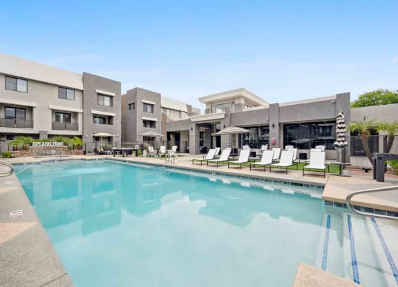 a swimming pool with chaise lounge chairs and umbrellas in front of a building