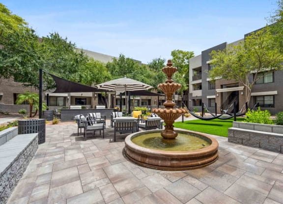 a fountain in the middle of a patio with chairs and umbrellas