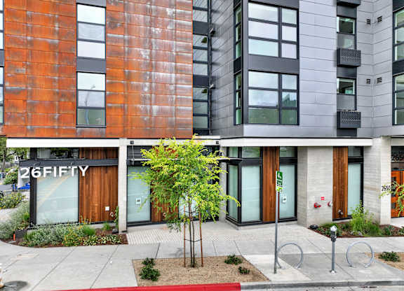 A modern building with a red brick facade and a tree in front at 26FIFTY Apartments, California