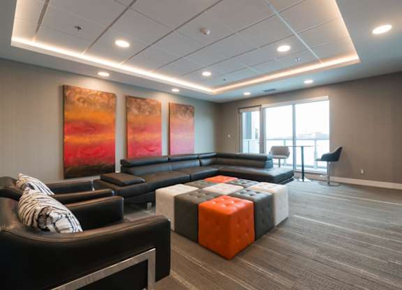 A modern living room with a black couch and a large painting on the wall.