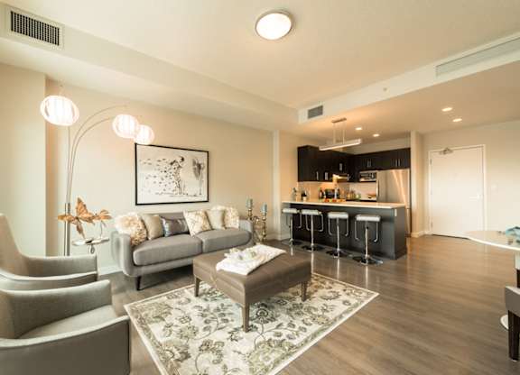 A modern living room with a grey sofa, a grey armchair, a coffee table, and a bar area in the background.