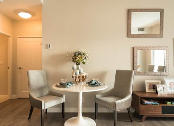 A dining room with a table set for two and a vase of flowers on the table.