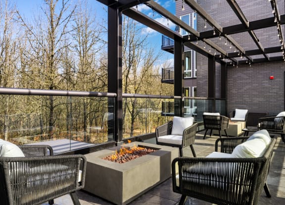 a covered patio with chairs and table and a fire pit over looking the forest