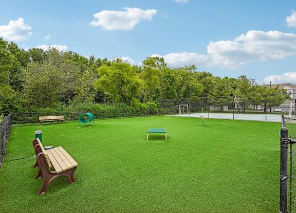 A green lawn with a wooden bench and a fence.