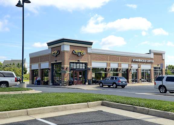 A Starbucks Coffee shop is located in a plaza with cars parked in front.