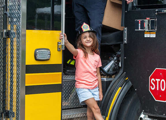 A little girl is standing on the step of a fire truck.