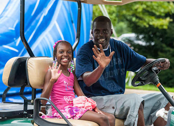 A man and a girl are sitting in a vehicle and waving at the camera.