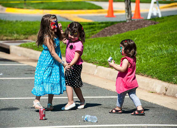 Three little girls playing with a bottle in a parking lot.