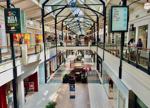 A busy shopping mall with people walking around and stores on either side.