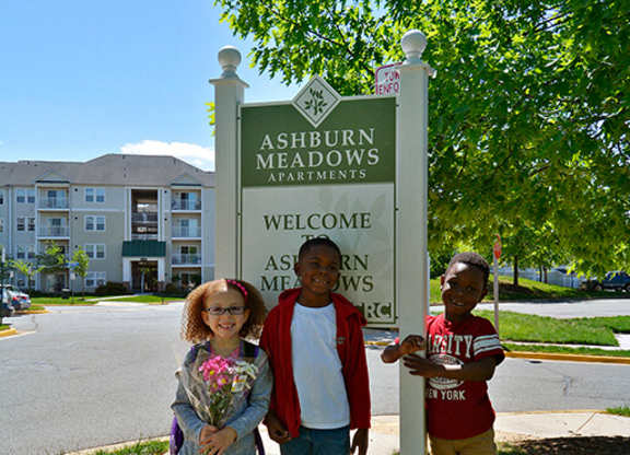 Three children stand in front of a sign that says Ashburn Meadows.