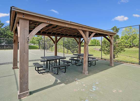 A wooden pavilion with a picnic table is situated on a tennis court.