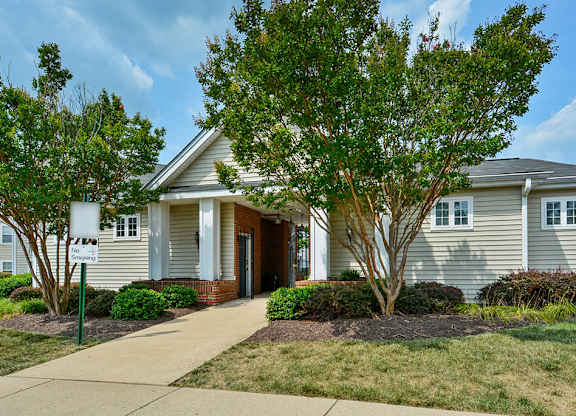 A house with a grey siding and a brown door is surrounded by green trees.